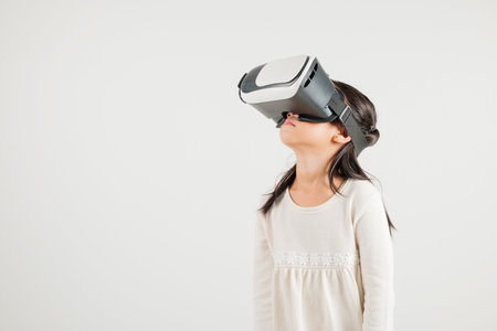 Smiling young kid girl confidence excited wear VR headset device during virtual reality experience isolated white background, Asian happy portrait kindergarten child playing video game studio shotの写真素材