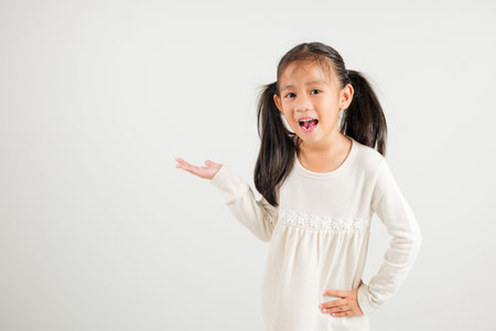 Asian happy portrait cute young girl smile presenting product holding something on palm away side, studio shot isolated on white background with copy space, kindergarten child show hand gestureの写真素材