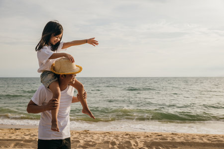 Happy family in holiday. Father and kids having fun together shoulder ride on summer beach, Parents carrying children on neck at beach, family is enjoying their summer in sunset timeの写真素材