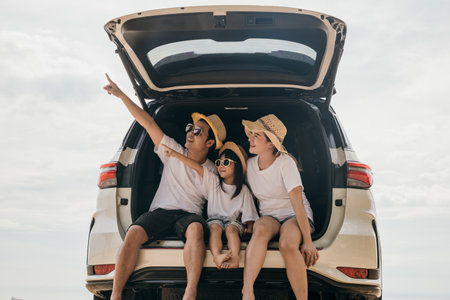Family Day. Father, Mother and daughter enjoying road trip sitting on back car and point finger out blue sky, Happy people having fun in summer vacation on beach, Family travel in holiday at sea beachの写真素材