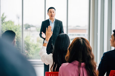 In a corporate setting, business professionals in a conference raise their hands for questions,...