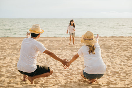 Asian little girl running into family open arms on beach. Happy father and mother welcomes cute daughter enjoying on sandy beach. summer outdoor activities conceptの写真素材