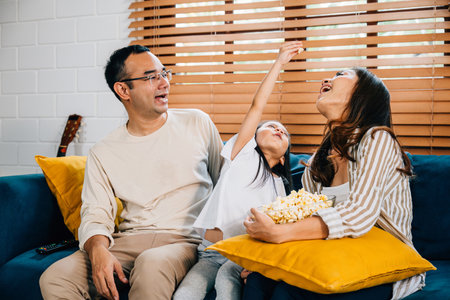 Heartwarming family scene unfolds as they watch TV with popcorn on sofa. father mother daughter and sibling radiate happiness and togetherness creating cherished memories during their time together.の写真素材