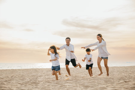 Smiling father and mother with son and daughter enjoying a carefree beach day. Running playing and laughing together creating memories of happiness family time and vitality. Family on beach vacationの写真素材