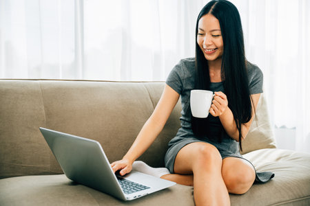 Woman on comfy sofa enjoys remote education laptop coffee. Embracing learning relaxation in a cozy living room. Networking and learning remotely. Comfortable education spaces.の写真素材