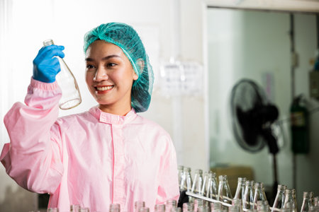 Worker in chemical science a QC woman in uniform meticulously examines glass bottles quality for...