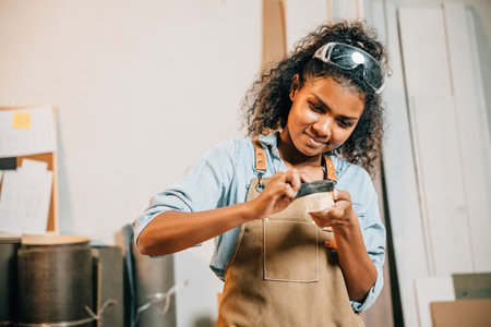 African American carpenter woman sanding a piece of wood. Wood grinding with sandpaper as she...