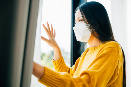Illustrating home quarantine, Woman in a medical mask practices self-isolation at home emphasizing COVID-19 prevention during the outbreak situation.の写真素材