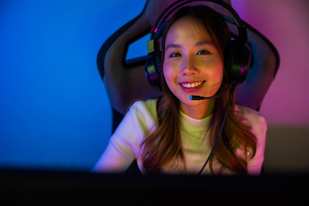 Asian happy Gamer endeavor plays online video games tournament with computer neon light, Smile young woman wearing gaming headphones intend to do playing live stream games online at home, font viewの写真素材