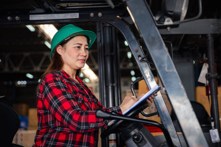 Adult female engineer depicted Asian woman confidently operates forklift truck at factory showcasing expertise in industrial occupation effectively managing tasks within industrial warehouse setting.の写真素材