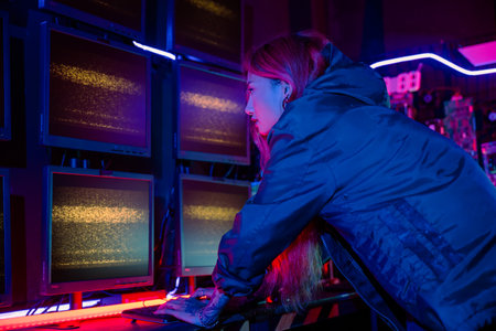 Asian woman wearing a black jacket hacking programming system and working with computer monitor display in dark office, Cyber security agency developing website cyber security, Monitoring Informationの写真素材