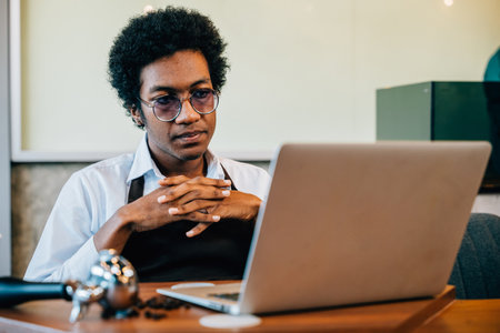 Entrepreneur also barista carefully inspects coffee beans using laptop in modern roastery office. Utilizing technology for meticulous checks ensuring premium bean quality. Owner assurance is evident.の写真素材
