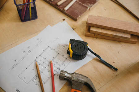Wooden surface with tape measure, hammer, pencils, and blueprint. Renovation tools and apartment plans laid out, perfect for home improvement, construction, and renovation concepts.の写真素材