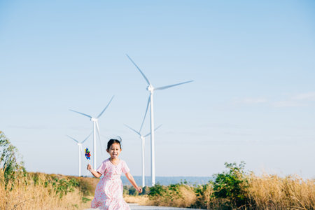 Childs playful exploration by windmills, little girl runs with pinwheels. Embracing wind energy education promoting clean electricity and sustainable industry in a beautiful setting.の写真素材