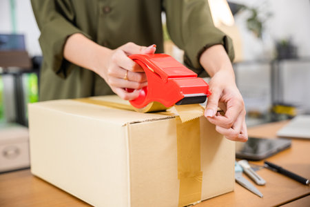 Close up woman hand packing shipment box with transparency tape at home office, happy freelance and packing cardboard box delivery products to customers, Startup small business, Moving dayの写真素材