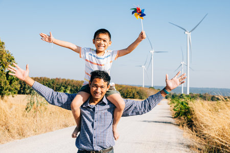 Father happily carries daughter with pinwheel. Family fun near windmills showcases global innovation in renewable energy. A joyful bonding moment in the community. Father Day Conceptの写真素材