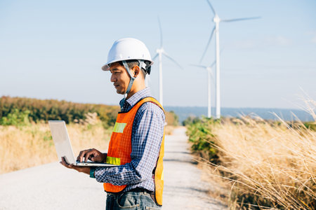 An engineer laptop in hand near windmills. Service technician ensuring turbine efficiency. Innovation in landscape development confidence in quality service and windmill repair.の写真素材