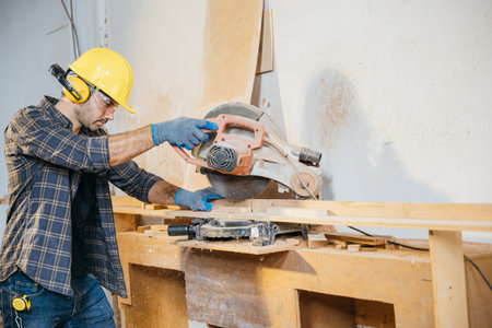 Man in a yellow hard hat using a circular saw to cut wood. Ideal for construction, home renovation, and woodworking, showcasing precise cutting techniques with power tools, National Carpenters Dayの写真素材
