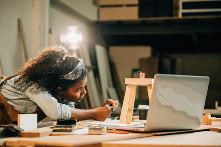 African American carpenter woman works on a wooden project using a laptop. utilize modern technology for designing new furniture, blending craftsmanship with digital tools, National Carpenters Dayの写真素材