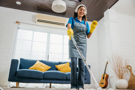 Asian teenager cleanup melody, maid sings dances with headphones. Joyful occupation in sync with music excitement. Modern cleaning technology vibe. Happy and Fun During Cleaningの写真素材