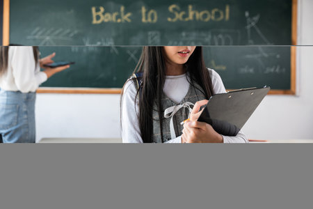 A girl is sitting in front of a blackboard with the words Back to School written on it. She is holding a clipboard and looking at itの写真素材