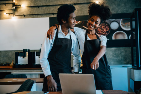 Two cafe owners plan supply orders on laptop in Coffee Shop. Black barista and owner discuss work schedule menu. Teamwork in cafe discussing finance business success on computer.の写真素材