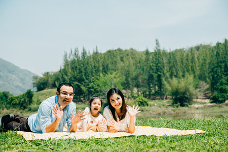 Asian family father mother and daughter lying on blanket spring meadow field grass in park cheerful sweet kid girl, parents and child picnic enjoying outdoors together, Family relaxation conceptの写真素材