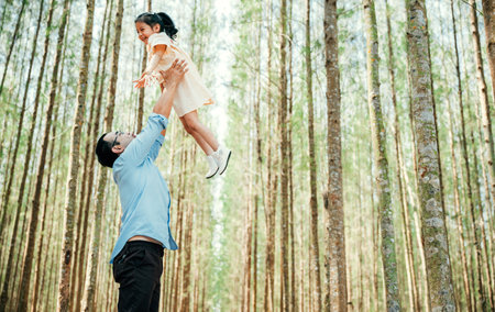 Playful family moment, father holds happy little girl up high, throwing up in sky at park forest. cheerful child enjoy moment playing freedom and joy, while loving dad captures precious memory foreverの写真素材