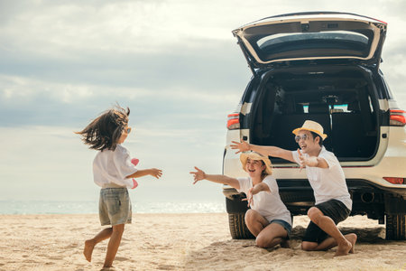 Asian family of three is playing on the beach on back car, with a young girl running towards car. Father and mother open their arms to welcome their daughter running towards them, summer trip conceptの写真素材