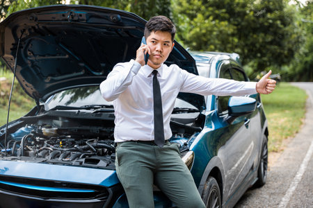 Man calling car insurance after vehicle breakdown on the road. Candid shot of businessman waiting for assistance with thumb up. Transportation and insurance concept.の写真素材