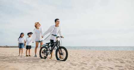 Parents walking on the sandy beach pushing their bicycles a scene full of family joy smiles and the inspiration of a carefree childhood. Family on beach vacationの写真素材