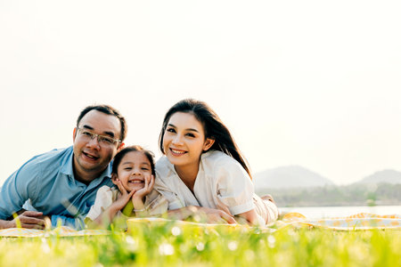 Asian family father mother and daughter lying on blanket spring meadow field grass in park cheerful sweet kid girl, parents and child picnic enjoying outdoors sunset time together, Family relaxationの写真素材