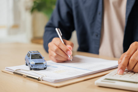 Signing and calculating car loan details, a man completes vehicle documentation. Ideal for financial transactions, tax planning, and securing contracts for new or used cars.の写真素材