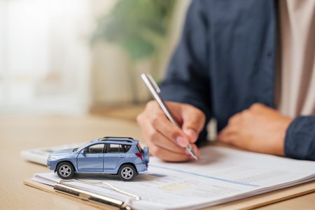 Signing a vehicle lease or insurance document, a man finalizes the purchase. Reflects auto finance, loans, rent agreements, and dealership services for new or used cars.の写真素材