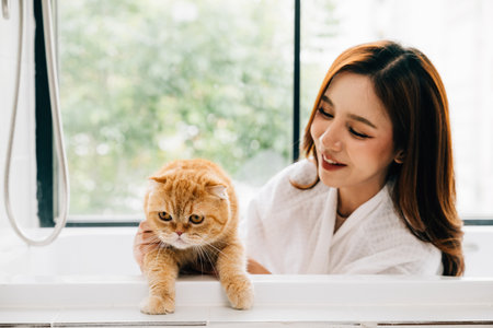 A womans bathroom retreat includes quality time with her Scottish Fold cat in the tub, portraying the joy of owner-pet love and happiness.の写真素材
