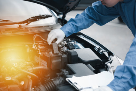 Auto technician in a workshop writing on a clipboard checking cars engine for maintenance. Mechanic...