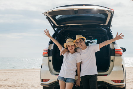 Asian couple is posing in back of a car enjoying beautiful views on the ocean beach. lifestyle man and the woman is wearing hat. Scene is relaxed and carefree, love and travel summer trip conceptの写真素材