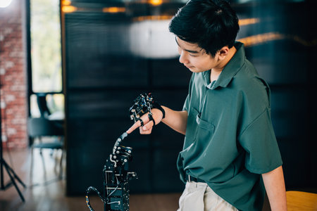 At a technical college a teen boy learns technology by testing a robot hand and arm touching fingers for educational skill enhancement. Embracing AI and futuristic humanity.の写真素材