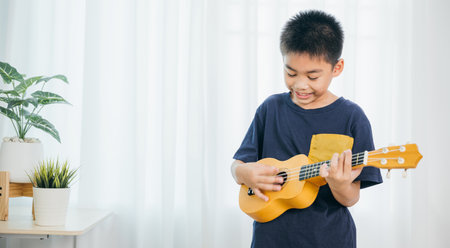 In a cozy living room, a young boy in a blue shirt strums a yellow ukulele, his face full of joy....