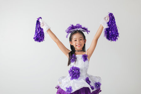 Portrait of a young cheerleader girl with purple pom-poms and a big smile. Her white and purple outfit adds to the festive, energetic mood. cheerleader kidの写真素材