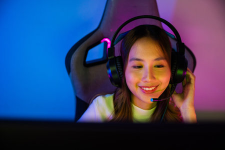 Asian happy Gamer endeavor plays online video games tournament with computer neon light, Smile young woman wearing gaming headphones intend to do playing live stream games online at home, font viewの写真素材