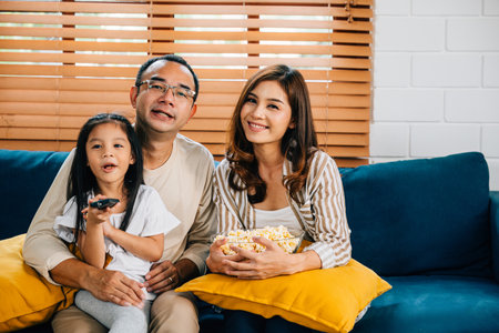 Enjoying quality family moments the family watches a video in their comfortable living room with popcorn. The father mother son daughter and schoolgirl share laughter joy and togetherness.の写真素材