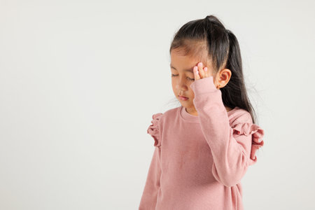 Portrait of Asian young kid girl sad tired strain face holding hold head by hands, stress kindergarten child person unhappy closed eyes problem headache, studio shot isolated on white backgroundの写真素材