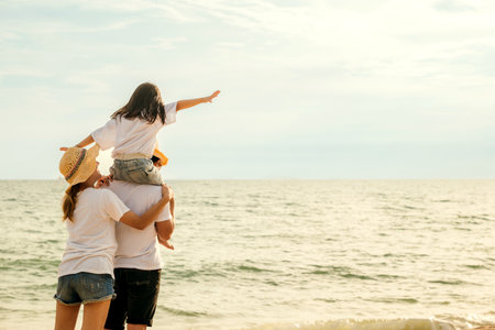 Happy family in holiday. Father, Mother and kids having fun together shoulder ride on summer beach, Parents carrying children on neck at beach, family is enjoying their summer timeの写真素材