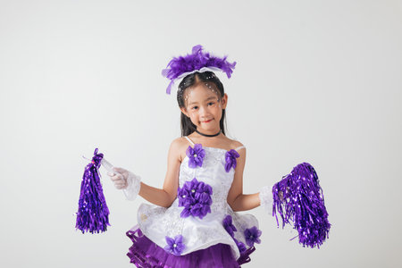 Excited kid in cheerleader uniform holds purple pom-poms. Studio shot on white background, full of cheer, fun, and playful energy. cheerleader kidの写真素材