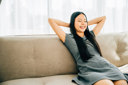 Serene woman on sofa hands behind head embraces relaxation. Dreaming and finding balance in a cozy home. Mindfulness wellbeing and comfort at its finest. Kick back and relax conceptの写真素材