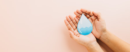 Hands hold a blue water droplet paper cut for World Water Day on pink background. Highlighting the importance of water, clean hygiene, and saving water to protect the environment.の写真素材