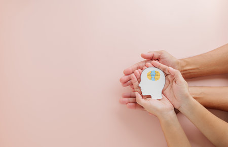 Adult and child hands hold a brain jigsaw in a head paper cut for Down Syndrome awareness. Celebrating Down Syndrome Day and Autism Awareness with a global message of hope on pink background.の写真素材