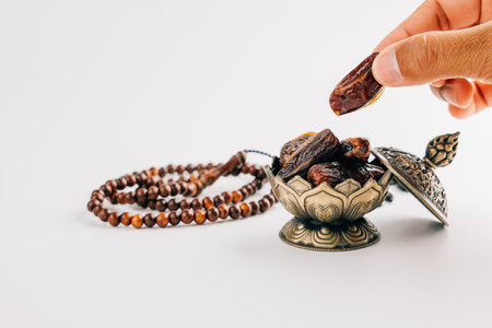 Holy Month of Ramadan. Hands hold dates fruit with ornate dish and beads on white background for Ramadan decoration and holy celebration.の写真素材