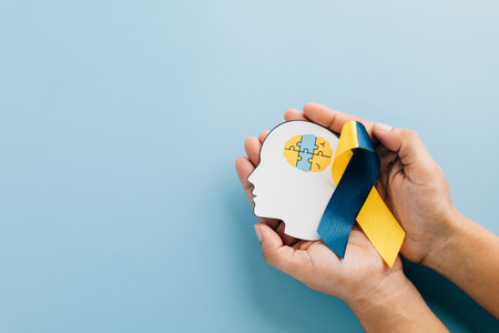 Supporting Down Syndrome, hands hold a head with puzzle pieces and a blue-yellow ribbon. Highlighting Autism Awareness and global Down Syndrome efforts on a vibrant blue background.の写真素材